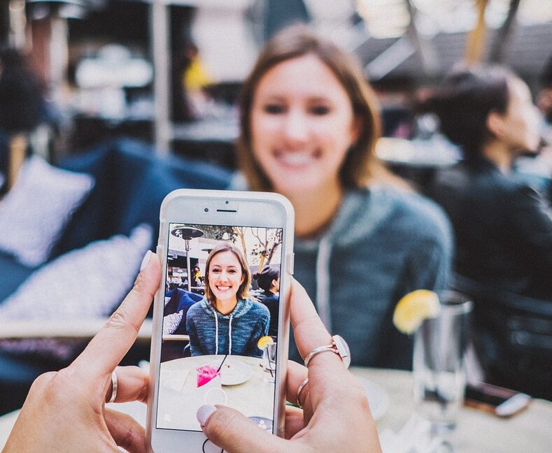 Wat is de invloed van social media op je zelfbeeld. Meisje kijkt lachend in de camera van haar telefoon.